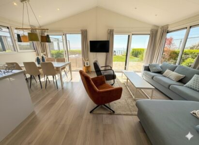 Modernes, helles Wohnzimmer mit Sofa, Esstisch und großen Fenstern mit Blick auf Garten und Meer. - Villa Sea Side