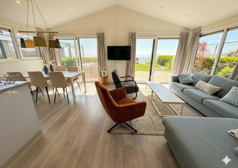 Modernes, helles Wohnzimmer mit Sofa, Esstisch und großen Fenstern mit Blick auf Garten und Meer. - Villa Sea Side