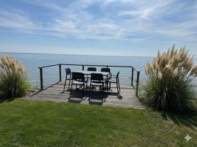 Holzterrasse direkt am Meer mit Tisch und Stühlen, Blick aufs ruhige Wasser und Schilfgras am Ufer. - Villa Sea Side