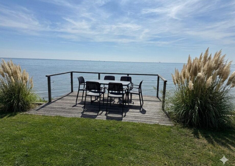 Holzterrasse direkt am Meer mit Tisch und Stühlen, Blick aufs ruhige Wasser und Schilfgras am Ufer. - Villa Sea Side
