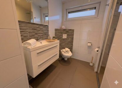 Helles, modernes Badezimmer mit Waschtisch, Spiegel, WC und Glasdusche in der Villa Sea Side.