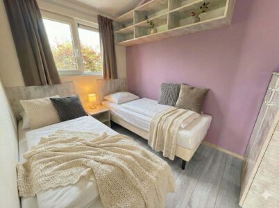 Helles Zweibettzimmer mit zwei Einzelbetten, lila Akzentwand, Fenster und Nachttischlampe in moderner Einrichtung. - Villa Sea Side