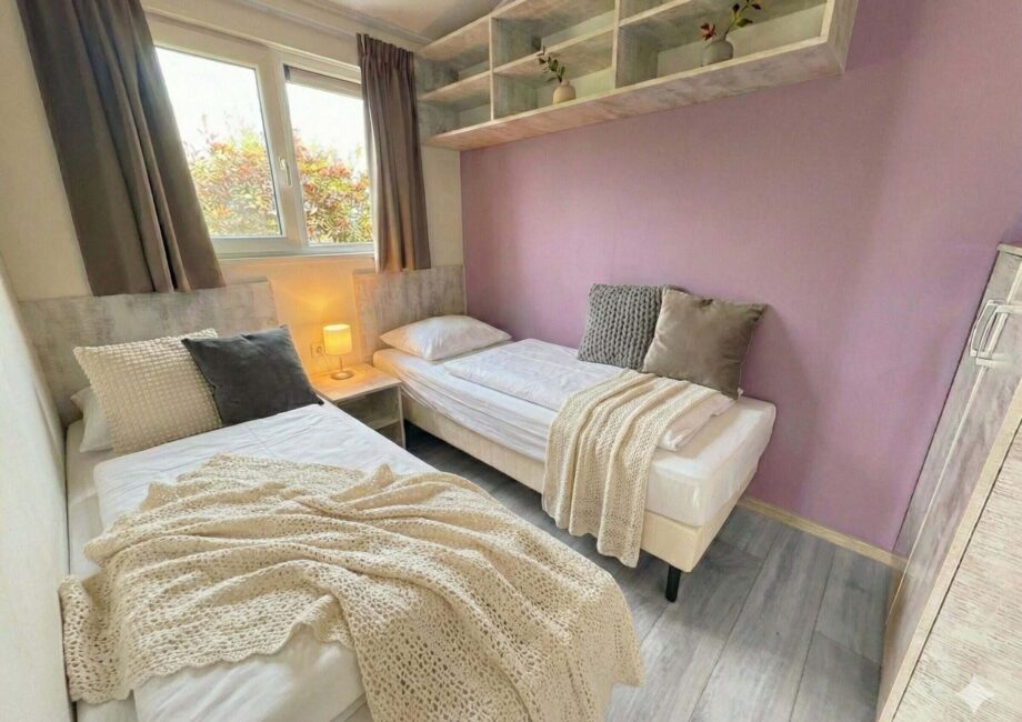 Helles Zweibettzimmer mit zwei Einzelbetten, lila Akzentwand, Fenster und Nachttischlampe in moderner Einrichtung. - Villa Sea Side