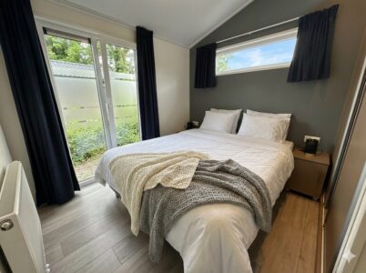 Modernes Schlafzimmer mit Doppelbett, weißen Kissen, dunklen Vorhängen und Terrassentür mit Blick ins Grüne. - Villa Sunset Beach