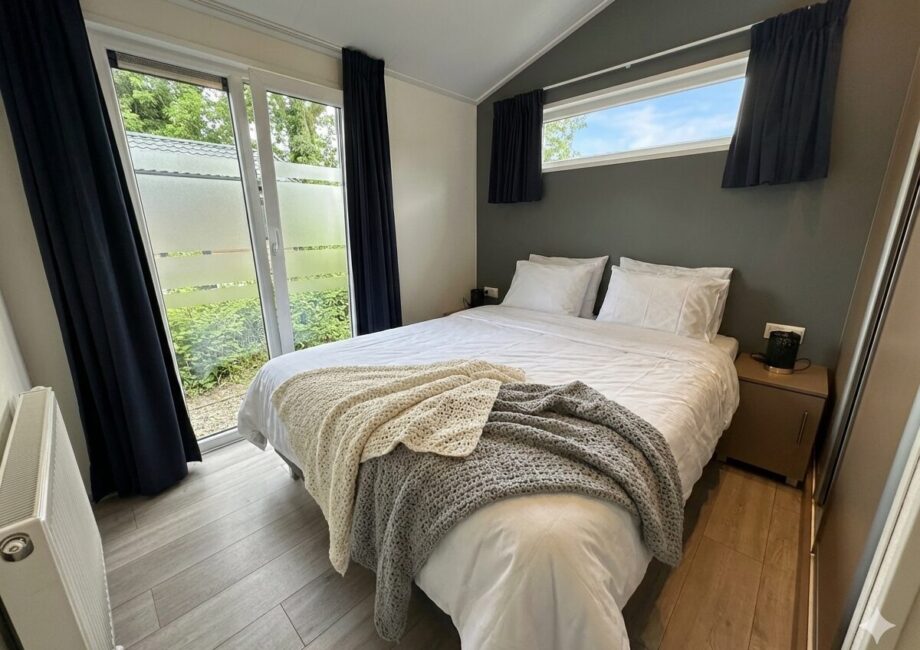 Modernes Schlafzimmer mit Doppelbett, weißen Kissen, dunklen Vorhängen und Terrassentür mit Blick ins Grüne. - Villa Sunset Beach