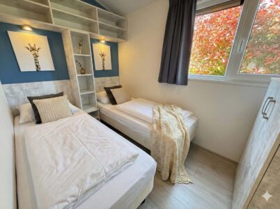 Helles Zweibettzimmer mit zwei Einzelbetten, Regalen, Giraffenbildern und Fenster mit Blick auf Herbstlaub. - Villa Sea Side