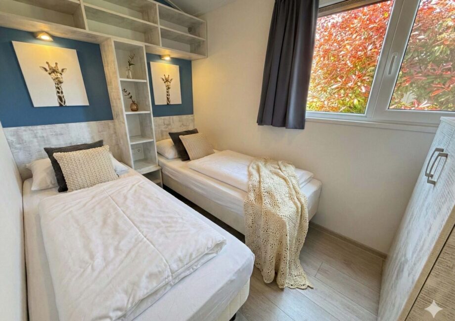 Helles Zweibettzimmer mit zwei Einzelbetten, Regalen, Giraffenbildern und Fenster mit Blick auf Herbstlaub. - Villa Sea Side