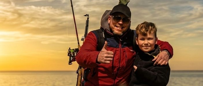 Vater und Sohn mit Angelruten bei Sonnenuntergang an der Küste